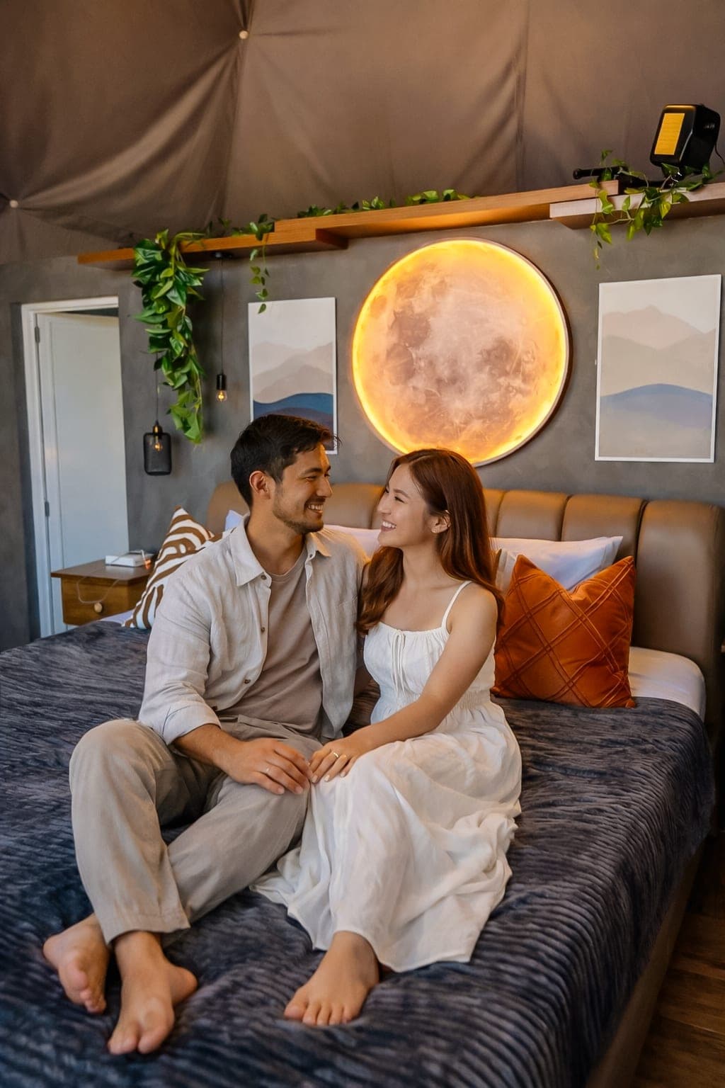 Two guests sitting on the bed beneath a round moon lamp